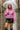 Woman in mauve acid wash hoodie, black leather skirt and rain boots, holding umbrella in city rain
