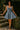 Woman in a denim dress standing on stone steps with greenery in the background