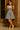 Woman wearing a denim dress with a bow detail standing against a wooden door.