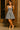 Woman wearing a denim dress with a bow detail standing against a wooden door.