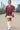 Woman walking in Mix Paisley Boho Tunic Blouse Color: Wine Mix with white mini skirt and boots, rooftop city view.