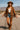 Woman in Mocha suede blazer with fringe, denim shorts and cowboy boots, on desert road, bright sunlight