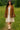 Woman in Mocha suede blazer with fringe, beige lace dress and light cowboy boots, in grassy field, daylight