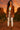 Woman in Mocha suede blazer with fringe, light leggings and sneakers, at red rocks, sunset glow