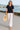 Woman strolling seaside in navy lace short sleeve shirt with white trousers and straw hat, morning sun