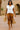 Woman walking in desert villa courtyard in off-white ribbed sweater vest with tan shorts, sunny midday