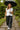Model walking on stone path in off-white ribbed sweater vest with charcoal wide-leg pants, garden rain
