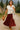 Woman walking on stone path in off-white ribbed sweater vest with red polka-dot skirt, countryside morning