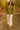 Woman in olive green shirt with jacquard hearts, beige pants and woven bag, walking in olive grove