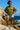 Woman in olive green shirt with jacquard hearts, denim shorts and sneakers, on seaside rocks