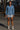Woman in denim paisley shirt and silver sequin skirt standing in front of steel beams