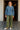 Woman in paisley denim shirt and olive pants with scarf in front of café
