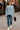 Woman walking in Oversized Sweater with Side Slit, blue jeans and white sneakers, holding black cap, city cafe background