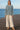 Woman in Oversized Sweater with Side Slit, cream wide-leg pants and beige sandals, standing on wooden pier by ocean