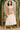 Standing East Asian woman in beige vest and tiered cream midi skirt with sandals, archway garden, soft light