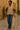 Walking Black woman in beige vest and flared jeans with leather strap bag, stone alley, warm evening light