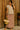 Standing South Asian woman in beige vest and red floral maxi skirt with raffia bag, wood wall, sunset light