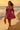 Walking barefoot on beach in paisley off-shoulder dress with seashell necklace and straw hat, sunset glow