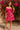 Posing by bougainvillea in paisley off-shoulder dress with pink heels and velvet headband, stone wall