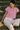 Sitting on stone steps in pink embroidered blouse with wide-leg cream pants, dappled sunlight