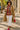 Woman in a plaid shirt and tan coat holding a coffee cup on a sidewalk.