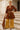 Woman posing on palace steps in red-brown corduroy mini dress with gold wide-leg pants and turban, sunny day