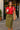 Smiling with coffee in red polo sweatshirt, olive button skirt and flats, café entrance, morning light
