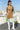 Fashion model standing in ribbed long sleeve mini sweater dress latte with white boots, rooftop daylight.