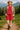 Woman in ruby ribbed outfit with boots and straw hat, walking in mountain meadow, daylight