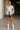 Woman in silver satin shirt with gray shorts, white socks and heels outside office building