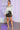 Woman in satin shirt and glitter skirt holding clutch in purple neon-lit gallery