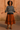 African American model in striped knit top with rust skirt, clogs, and headband against adobe wall