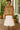 Woman in striped sweater layered over white dress and sandals smiling on wooden porch