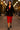Woman in a black blazer and red dress walking on a street with blurred lights in the background