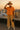 Holding hat in textured cotton-blend shirt with wide-leg pants and heeled boots, rooftop, sunset