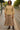 Woman standing in taupe textured knit V-neck top with tiered skirt and boots, tram stop street scene.
