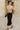 Model walking in sand beige tie front cropped sweater vest with black satin skirt, old town street daylight.