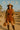 Rust ribbed knit set styled with camel coat, suede boots, and round woven bag in desert setting