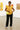 Posing in art gallery in yellow floral blouse with black trousers and neon sneakers