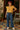 Standing on tiled porch in yellow floral blouse with flared jeans and sneakers, polka dot headband