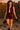 Model posing in maroon zip front vest with leather shorts and loafers, ancient ruins at sunset.