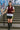 Smiling woman in maroon zip front vest with graphic tee and biker shorts, city stairs graffiti wall.