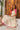 Woman in a white dress with pink accents sitting on pebbles next to a wooden door.