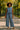 African American woman in blue two-piece set, straw hat, walking through sunny park path.