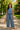 Latin American woman in blue summer set with straw tote and sandals in sunlit park.