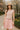 Woman in blush knit sweater and pink tiered dress wearing a straw hat in spring park