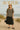 Woman in floral babydoll blouse with straw hat and black skirt on a sandy beach