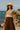 Woman in mocha striped knit sweater and brown skirt by the ocean under a sunhat
