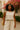 Woman in linen jumpsuit with straw bag walking past pink blooms