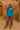 Woman in blue blouse, tribal print pants, and round bag in desert setting